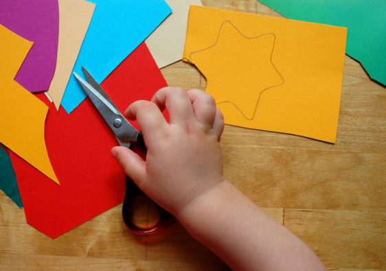 Ein Bild von einer Kinderhand mit einer Schere und Bastelmaterial