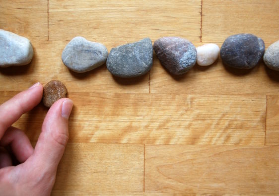 Foto von einer Hand, welche eine Reihe aus Steinen legt