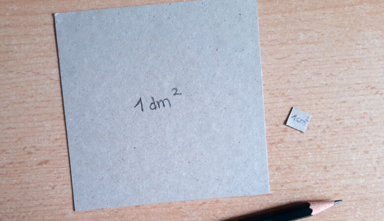 Foto von einem Pappstück, welches genau einen Quadratdezimeter groß ist, und einem Pappstück, welches genau einen Quadratzentimeter groß ist.