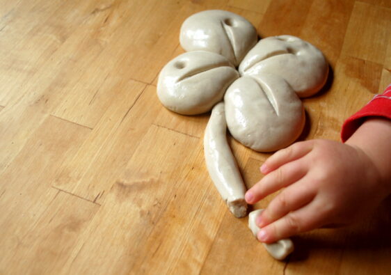 Foto von einer Kinderhand, die aus Knete ein vierblättriges Kleeblatt formt. Symbolfoto zum Thema Aberglaube