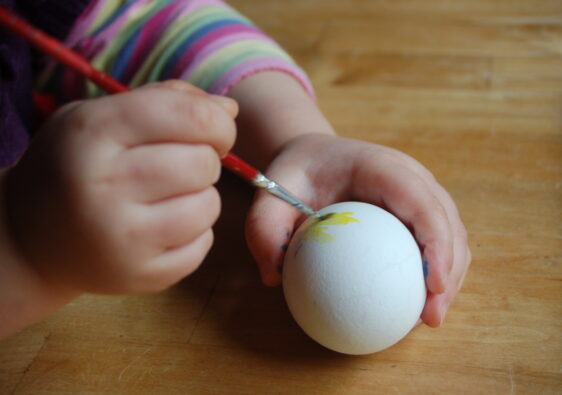 Ostereier anmalen: Foto von einem Kleinkind, welches mit einem Pinsel ein Osterei bemalt