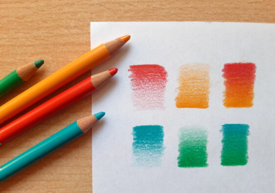 Auf dem Schreibtisch liegen Buntstifte und ein Blatt Papier, auf dem versucht wurde, die Farben der Buntstifte miteinander zu verblenden