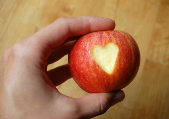 Ein Foto von einer Hand, die einen Apfel hält, in den ein Herz eingeschnitzt ist. Symbolbild für die Beziehungsarbeit in der Schule.