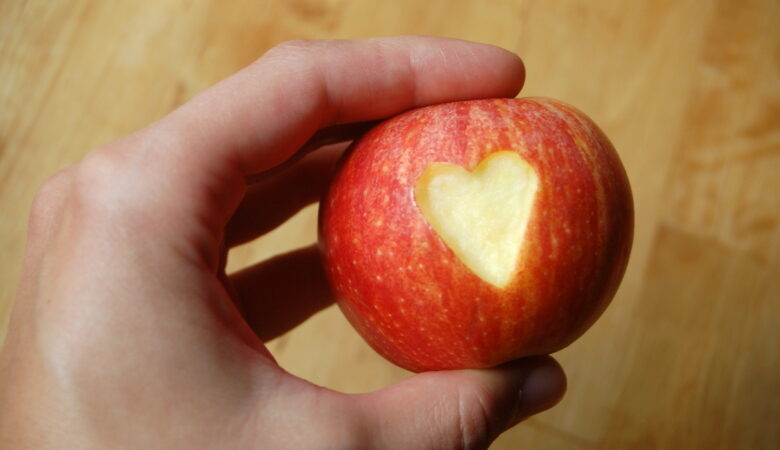 Ein Foto von einer Hand, die einen Apfel hält, in den ein Herz eingeschnitzt ist. Symbolbild für die Beziehungsarbeit in der Schule.