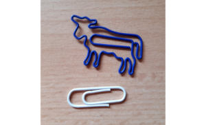 Ein Foto von einer blauen Büroklammer in Form einer Kuh (Schmuckform) und einer schlichten, weißen Büroklammer (Zweckform)