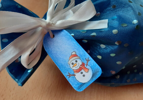 Dieses Foto zeigt ein blaues Geschenk mit einem selbstgebastelten Geschenkanhänger mit einem Schneemann (passend zu Weihnachten)