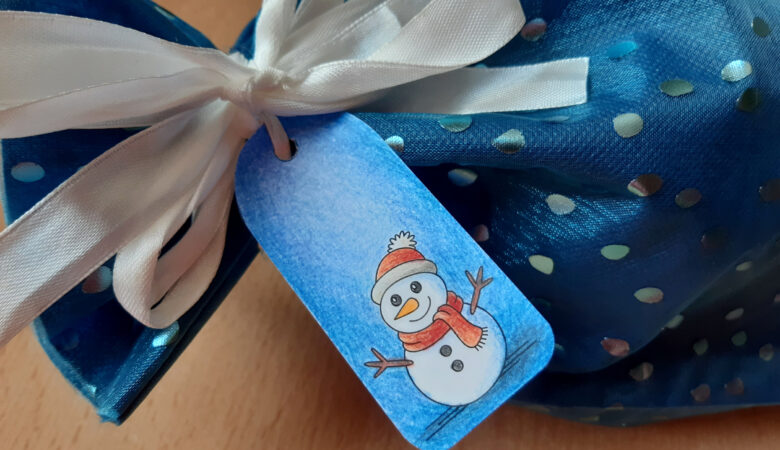 Dieses Foto zeigt ein blaues Geschenk mit einem selbstgebastelten Geschenkanhänger mit einem Schneemann (passend zu Weihnachten)